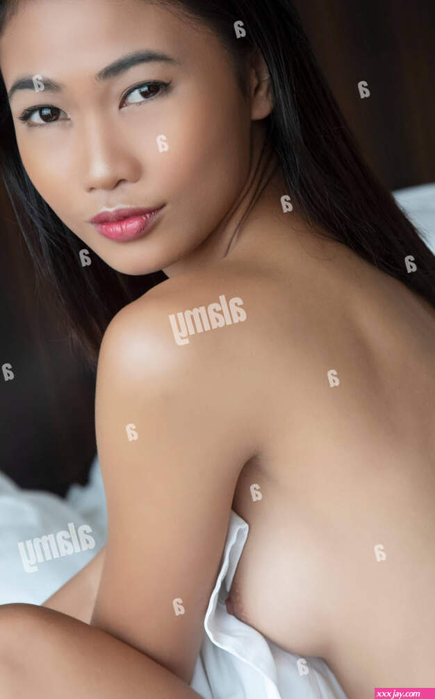 Beautiful Asian woman posing nude on a bed with white sheets Stock Photo